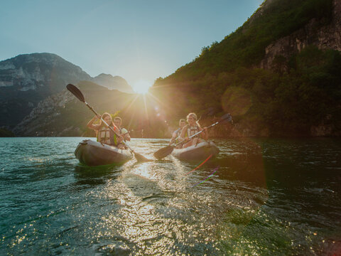A group of friends enjoying fun and kayaking exploring the calm river, surrounding forest and large natural river canyons during an idyllic sunset.