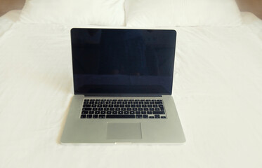 Laptop with blank black screen with smartphone and keyboard on white bed in the room