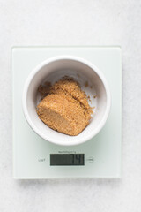 Brown sugar being weighed on a digital scale, sugar for baking in a ramekin