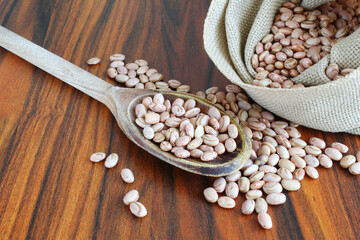Carioca beans in a wooden spoon with jute bag and beans scattered on the table.