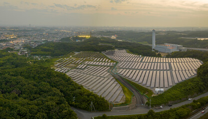 Aerial: Sunset light over panels on solar farm on edge of city