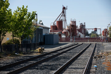 Fototapeta na wymiar Oakdale, California, USA - April 18, 2023: Afternoon sunlight shines on Industrial buildings and rail tracks in downtown Oakdale.
