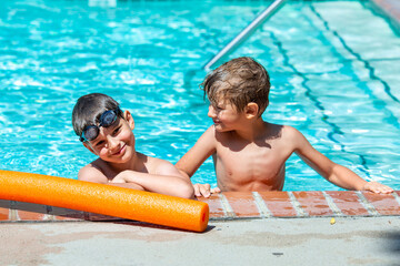 Oudoor summer activity. Concept of fun, health and vacation. A happy brothers boys eight and five years old in swimming goggles are holding onto the side of the pool on a hot summer day.