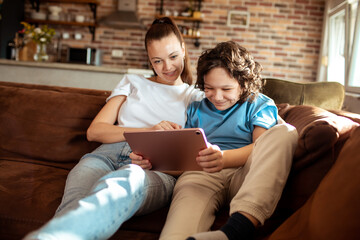 Mother and son using a digital tablet on the couch in the living room of their home