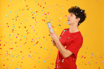 Happy teenage boy blowing up party popper on orange background