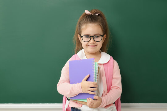 Happy little school child with notebooks near chalkboard