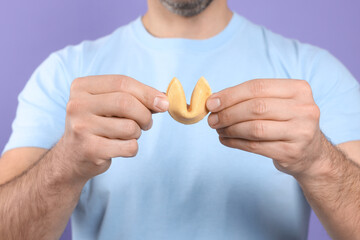 Man holding tasty fortune cookie with prediction on violet background, closeup