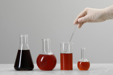 Scientist taking brown liquid with pipette from beaker at table against light background, closeup