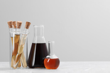 Different laboratory glassware with brown liquids on white table against light background. Space for text