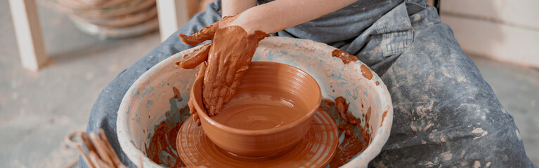 Young woman works on pottery wheel in atelier - obrazy, fototapety, plakaty