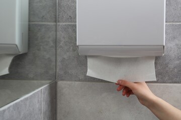 Woman taking new fresh paper towel from dispenser in bathroom, closeup. Space for text