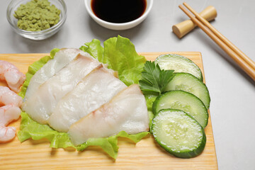 Sashimi set served with cucumber, lettuce, soy sauce and vasabi on light grey table, closeup