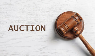 Word Auction and gavel on white wooden table, top view