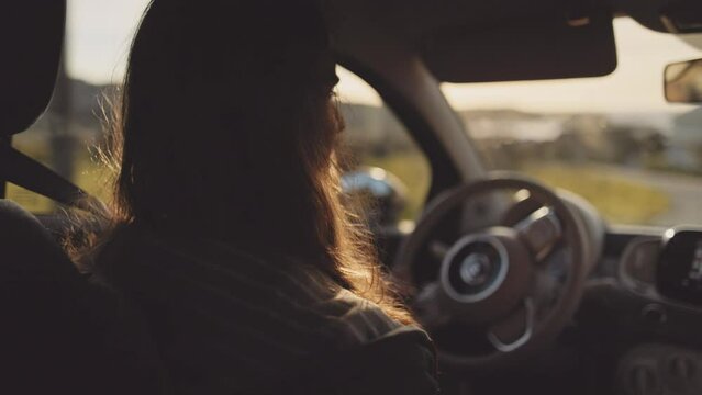 Man driving a car at sunset. Unrecognizable male driver holding steering wheel, sunrise, morning or evening road with lens flare. Young gen z man traveling in a vehicle, road trip. 