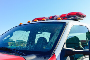 A red emergency firetruck with a lightbar on the roof. The lights are red, orange, and white color. The rescue pick-up truck has a white roof and a red painted bonnet. The background is a blue sky.