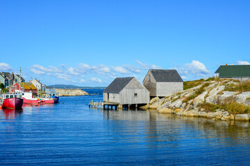 Fototapeta na wymiar Scenic Peggy's Cove, Nova Scotia, is a quaint fishing village on the edge of a rocky coastline. The storage buildings are grey and weathered. The summer sky and water are blue with white clouds. 