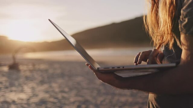 Man with laptop works on the ocean beach. Unrecognizable person freelancer with remote digital online job on the seaside, using computer technology and internet. 