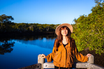 Portrait of beautiful smiling girl wearing hat with mangrove forest and river in background. Nudgee...