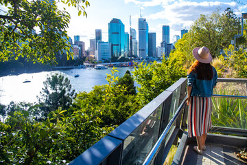 beautiful woman in a hat enjoying panorama of brisbane cbd from kangaroo points; brisbane skyline and river seen from famous cliffs, holidays in brisbane - obrazy, fototapety, plakaty