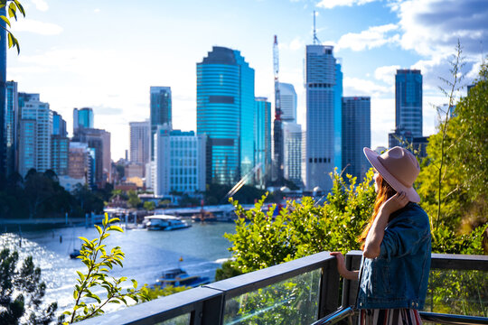 beautiful woman in a hat enjoying panorama of brisbane cbd from kangaroo points; brisbane skyline and river seen from famous cliffs, holidays in brisbane