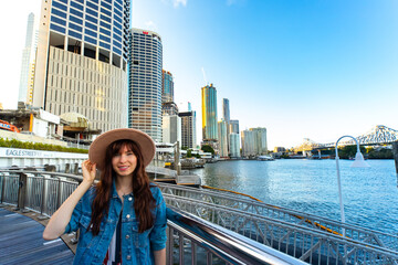 Obraz na płótnie Canvas portrait of a beautiful girl standing on the city reach boardwalk in brisbane cbd with large skyscrapers in the background; brisbane skyline byt the river, australia