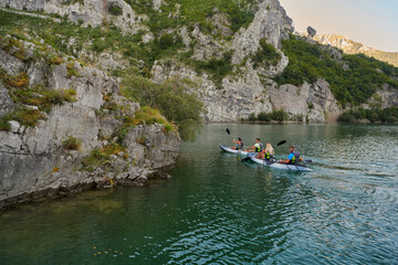 Naklejka na ściany i meble A group of friends enjoying having fun and kayaking while exploring the calm river, surrounding forest and large natural river canyons
