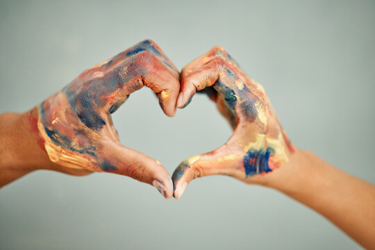 We love doing everything together. Cropped shot of a couple forming a heart shape with their hands while painting.