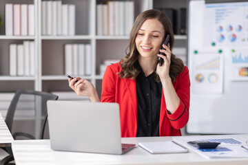 Obraz na płótnie Canvas Cheerful business Asian Canadian woman freelancer making telephone call share good news about project working in office workplace, business finance concept. 