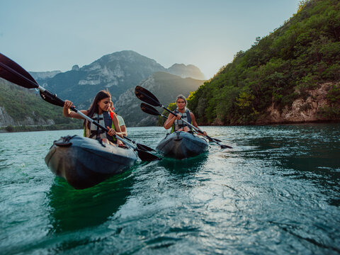 A group of friends enjoying fun and kayaking exploring the calm river, surrounding forest and large natural river canyons during an idyllic sunset.