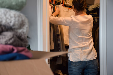 Woman from behind inside walk in closet sorting and organizing her clothes