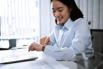 Portrait of  Asian Business woman watching at wristwatch while working on laptop computer in office. watching the time .working new start up project