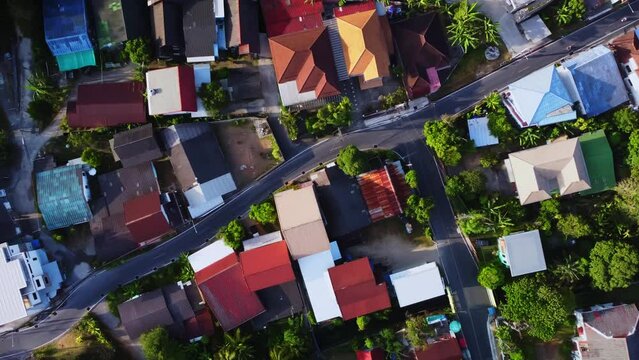 Top aerial drone footage of asian village with residential houses and asphalt road where motorcycles drive. Scenery of a town and way with left hand traffic filmed from above at warm summer day