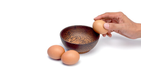 Cracking one of the three eggs on a wooden cup on a white background.