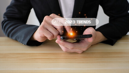 Businessman using smartphone to input keyword of 2023 trends inside infographic searching tool bar...