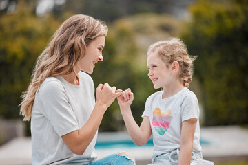 Fototapeta premium Happy young caucasian mother sitting with her adorable little daughter in the garden at home and making pinky promises. Cute little girl bonding with her parent in the backyard swearing to secrecy