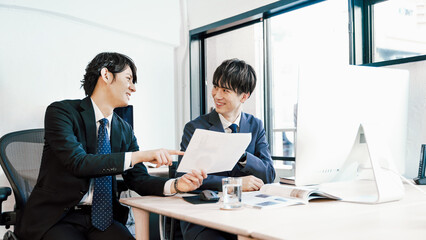 オフィスの社内で社員同士でアイデアを出し合う20代から30代の2人の若手社員の男性