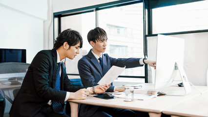 オフィスでパソコンへの入力内容を確認する若い2人のビジネスマンの男性