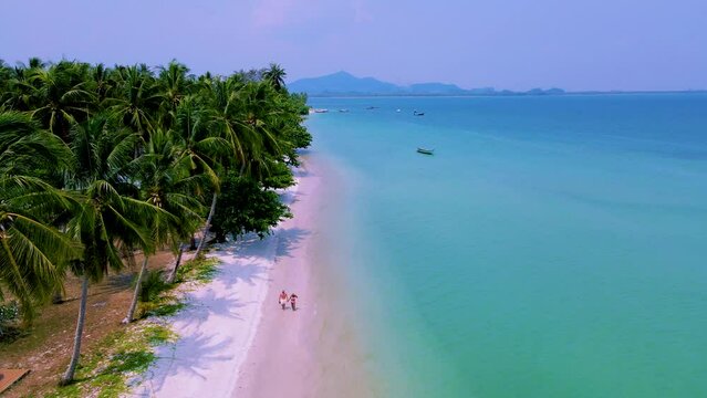 Koh Mook Island or Koh Muk Trat Thailand a tropical white beach with palm trees. A Couple of men and woman on vacation in Thailand walking at the beach