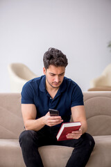 Young male student reading book at home