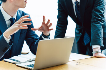 スーツを着た2人のビジネスパーソンの男性の机のノートパソコンの前での会議と相談と説明の手元のシーン