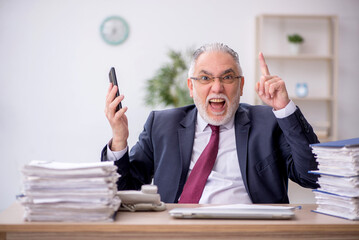 Old male employee speaking by phone at workplace