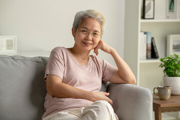 Portrait of smiling Asian senior woman sitting on sofa at home