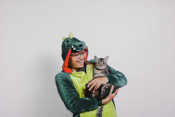 a man in a dinosaur costume poses happily holding a cat on a white background