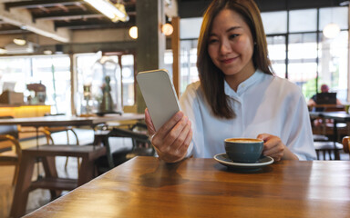 Portrait image of a young woman holding and using mobile phone while drinking coffee in cafe