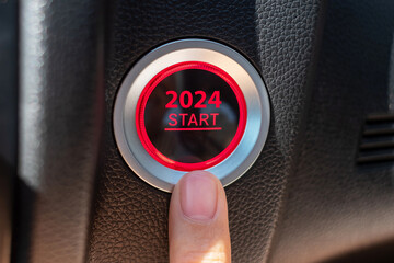 Finger press a car ignition button with 2024 START text inside  automobile. New Year New You, forecast, resolution, motivation, change, goal, vision, innovation and planning concept