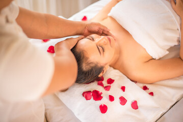 Obraz na płótnie Canvas Beautiful asian client lying on bed sprinkled with rose petals in spa room feeling refreshed and renewed her body and mind in perfect harmony.