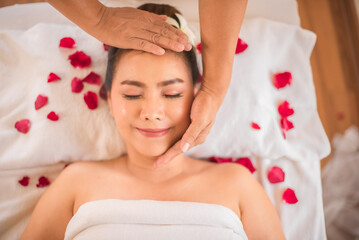Obraz na płótnie Canvas The soft hands of the masseuse's moving over the customer's head and cheek make her comfortable on bed sprinkled with rose petals in spa room.