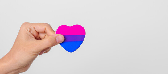 Bisexuality Celebrate Day and LGBT pride month,  LGBTQ+ or LGBTQIA+ concept. Hand holding purple, pink and blue heart shape for Lesbian, Gay, Bisexual, Transgender, Queer and Pansexual community