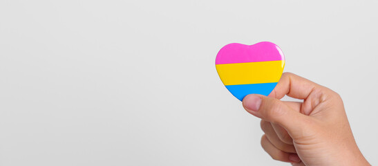 Pansexual Pride Day and LGBT pride month concept. hand holding pink, yellow and blue heart shape for Lesbian, Gay, Bisexual, Transgender, Queer and Pansexual community - obrazy, fototapety, plakaty