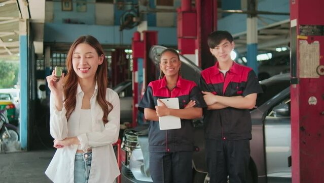 Young Asian female customer shows car key with automotive mechanic workers, happy smile in quality trust at maintenance garage, professional vehicle service center, fix check and repair auto industry.